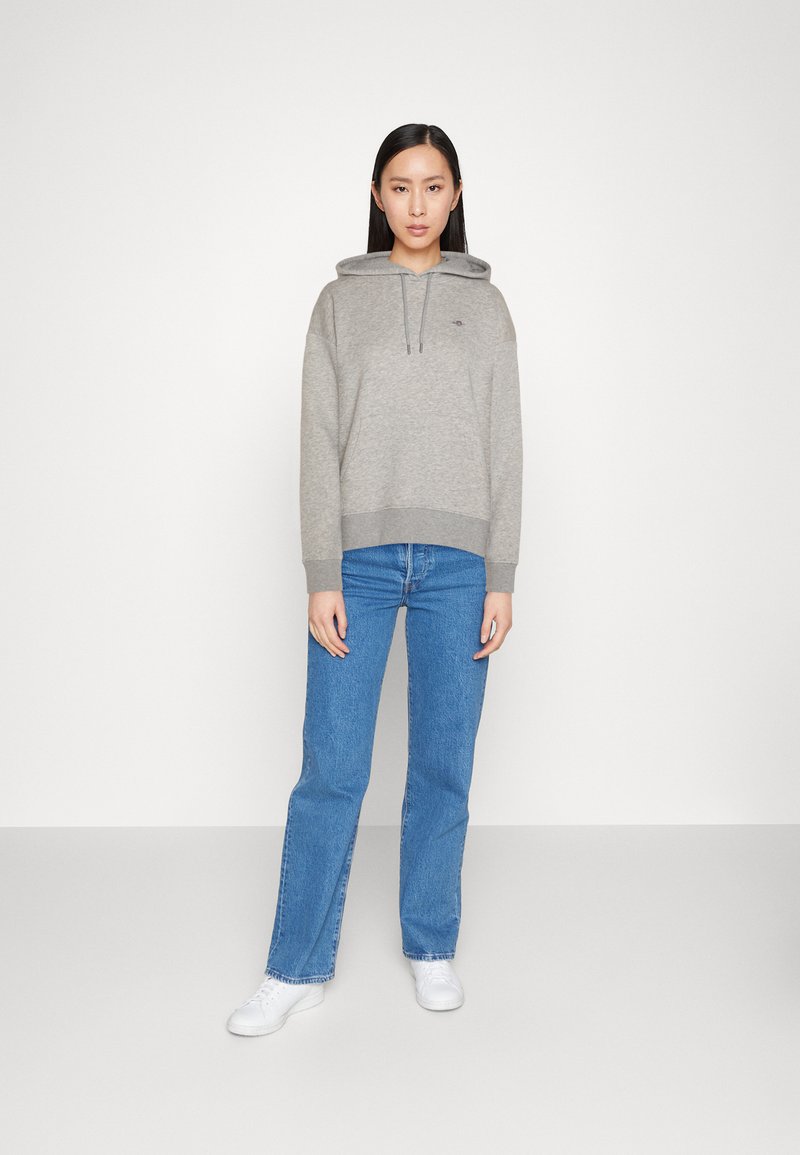 Un hoodie gris avec un cordon de serrage ajustable, des poignets côtelés et un ourlet côtelé. Associé à un jean droit bleu et des baskets blanches. Un design simple et décontracté.