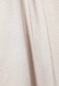 Tissu beige avec une surface douce et texturée, présentant un léger éclat et une belle drapé. Le tissu montre des vagues et des plis délicats.