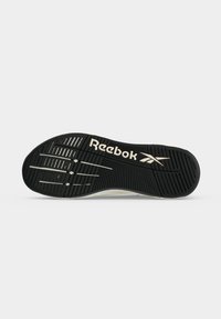 Σολά ενός μαύρου παπουτσιού Reebok με υφασμένους σχεδιασμούς για καλύτερη πρόσφυση και το λογότυπο Reebok σε λευκό κοντά στην περιοχή του αψιδωτού του ποδιού σε ανοιχτό γκρι φόντο.