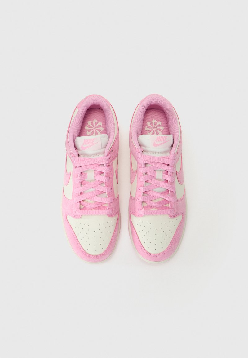Baskets Nike avec un dessus en daim rose et des accents en cuir blanc. Bout arrondi, lacets roses et motif floral sur la semelle intérieure.
