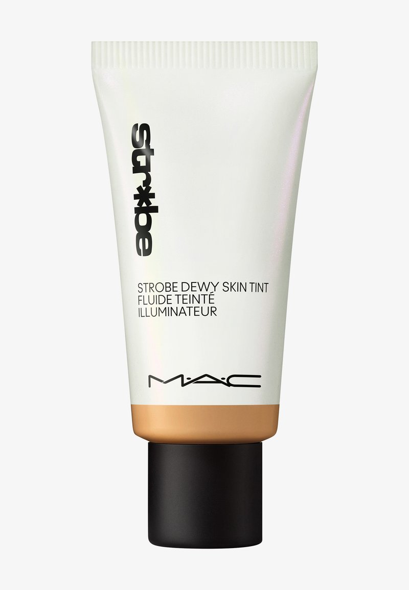 Valkoinen muoviputki kultapohjalla, jossa on mustaa tekstiä. Etiketti lukee "Strobe Dewy Skin Tint." Teksturoitu korkki on musta ja pyöreä.