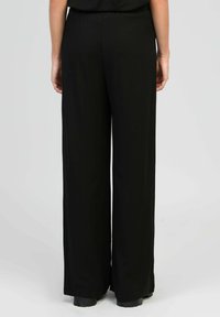 Pantalons larges noirs avec une texture lisse et une taille élastique. Présente une vue arrière montrant la longueur complète et un minimum de matériel.