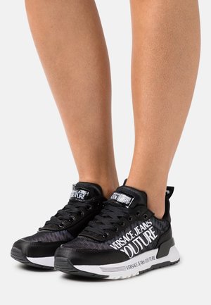 Czarne sneakersy z siateczkowym i syntetycznym wierzchem, białymi akcentami logo, teksturowanymi sznurówkami oraz grubą gumową podeszwą.