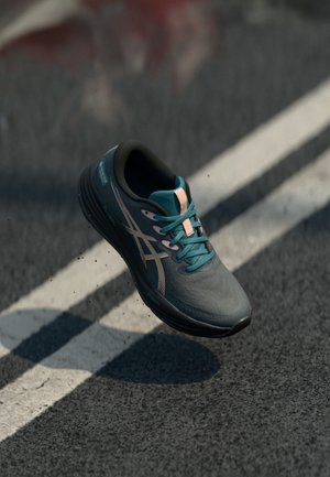 Scarpa atletica leggera grigia con tomaia testurizzata, lacci turchesi, accenti rosa e suola nera curva, con marchio sul lato.