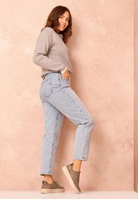 Hellblaue hochgeschnittene Jeans mit geradem Schnitt, kombiniert mit einem grauen Pullover und grauen Turnschuhen. Glatte Texturen und lässiges Design.