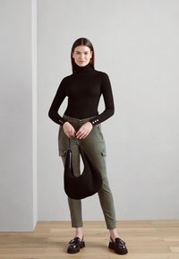 Svart ribbet turtleneck, olivenfargede cargo-bukser med sidelommer, og svart hobo-veske. Modellen har på seg svarte chunky loafers og har langt, rett hår.