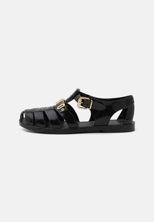 Black rubber sandals with cut-out design, featuring a gold buckle closure and textured insole. Stamped logo on the heel.