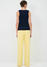 Top senza maniche blu abbinato a pantaloni larghi gialli con vita alta, caratterizzati da una texture morbida e un design minimalista.