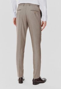 Beżowe spodnie w paski, o dopasowanym kroju. Posiadają tylne kieszenie zapinane na guziki. Gładka tekstura, w połączeniu z wypolerowanymi butami.