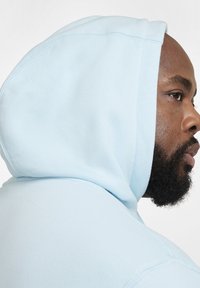 Felpa blu chiaro con una texture morbida, dotata di cappuccio con coulisse e dettagli di cucitura visibili lungo i bordi.