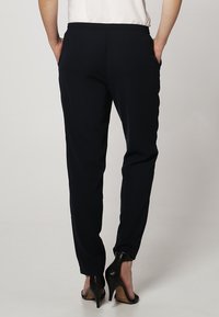 Granatowe spodnie z gładkiej tkaniny, o tapered design, z kieszeniami po bokach, zestawione z czarnymi szpilkami.
