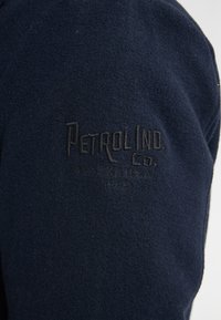 Giacca in lana blu navy con logo ricamato 'Petrol Inc. Co.' e dettagli vintage, dalla finitura morbida e testurizzata con taglio classico.