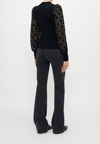 Maglione nero con maniche trasparenti a pois, polsini e scollatura in costina. Abbinato a jeans svasati grigio scuro. Texture liscia su tutta la superficie.