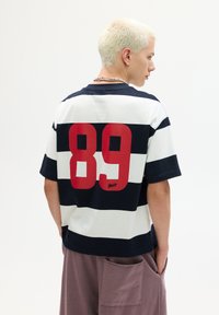 Navy and white striped short-sleeve T-shirt with a large red "89" graphic on the back and a signature detail at the bottom. Cotton material.