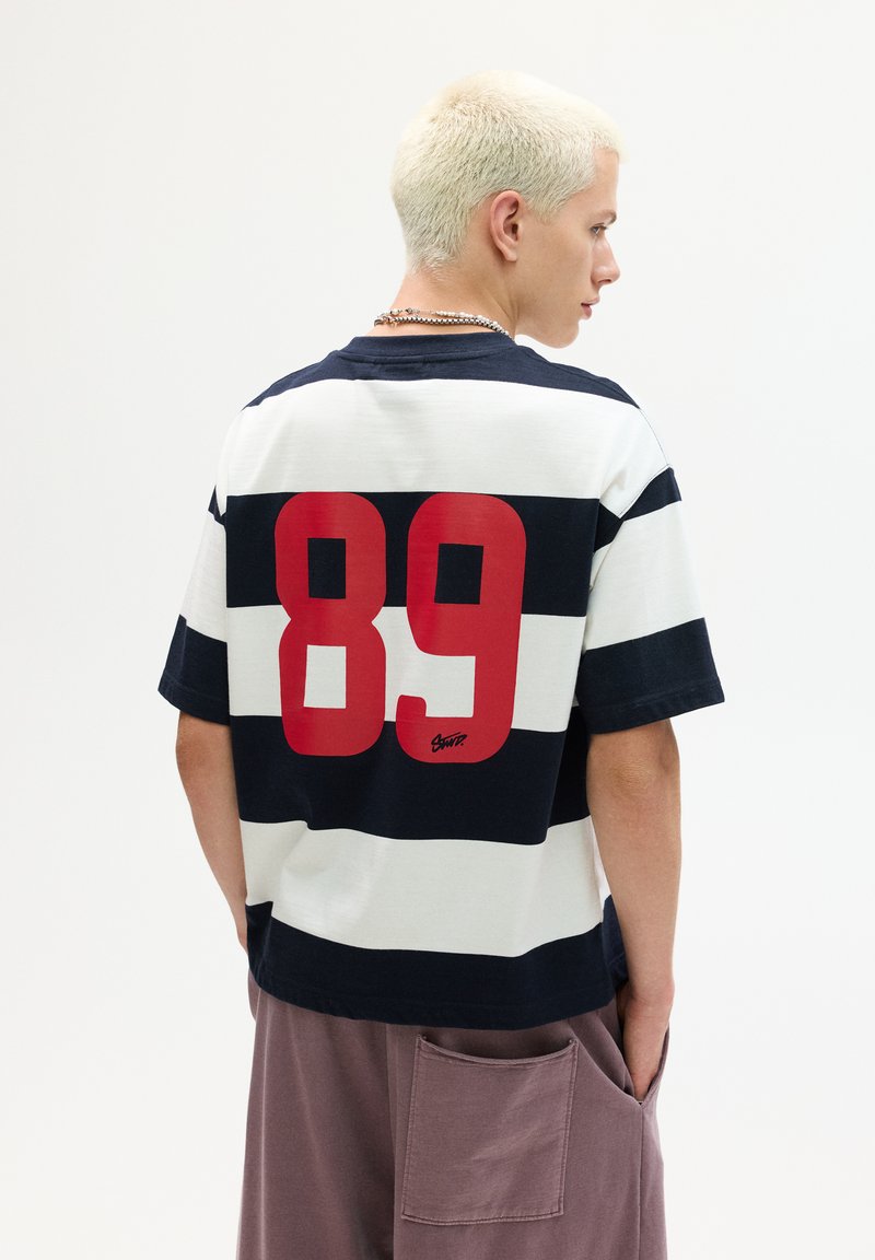 Navy and white striped short-sleeve T-shirt with a large red "89" graphic on the back and a signature detail at the bottom. Cotton material.