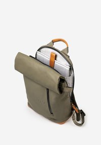 Zaino verde oliva con chiusura a rotolo, dettagli in pelle color cuoio, una tasca con cerniera e un interno testurizzato con motivo a griglia.