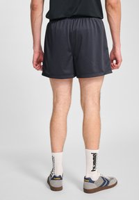 Svarta träningsshorts med en texturerad meshfinish, med en elastisk midja. Bärs med grå och blå sneakers samt vita strumpor.