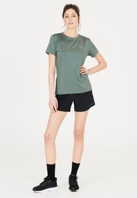 Grön sportt-shirt med en mjuk textur, ihopparad med svarta shorts. Har en rund halsringning och korta ärmar, designad för aktiv användning.
