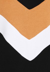 Pull avec un motif chevron composé de trois couleurs : noir, blanc et moutarde. Confectionné en tissu doux, mettant en valeur des textures et des formes contrastées.