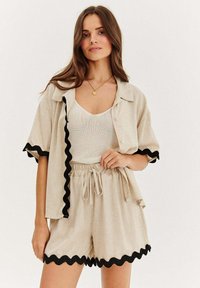 Lněný dvoudílný set obsahující košili s krátkým rukávem na knoflíky s černým vlnkovaným lemem a odpovídající šortky s elastickým pasem a vlnkovaným lemem.