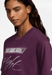 Lilla puuvillane T-särk, millel on hõbedane Nike logo ja "Flight" graafika esiküljel, lühikeste varrukatega ja ümmarguse kaelusega.