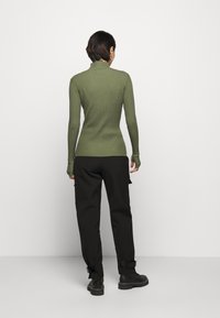 Geribbelde olijfgroene turtleneck trui met lange mouwen, gecombineerd met een hoge taille zwarte broek en stevige zwarte laarzen.