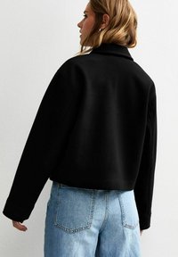 Sweatshirt noir court avec un col structuré et des manches longues, associé à un jean taille haute bleu clair. Texture lisse, design minimaliste.