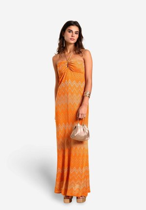 Mouwloze maxi-jurk in oranje met een chevronpatroon, geraffineerd bij de buste. Gecombineerd met een zilveren tas en chunky platformhakken.