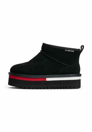 Bottines noires à finition en daim, avec une semelle épaisse à plateforme et des accents rouges et blancs, bout arrondi et boucle de tirage.