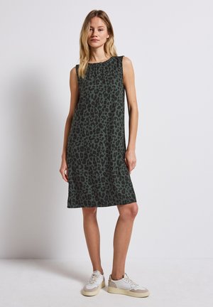 Vihreä hihaton mekko, jossa on musta leopardi-kuvio, löysä malli, polvipituinen, yhdistettynä valkoisiin ja beigeihin tennareihin.