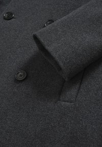 Mörkgrå ullkappared med ärmar och framsida, svarta knappar och en horisontell bröstficka.