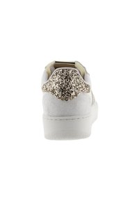 Sneaker bianco con lato testurizzato e accentuazione glitterata dorata sul tallone. Presenta una suola piatta, forma arrotondata e un design minimalista.