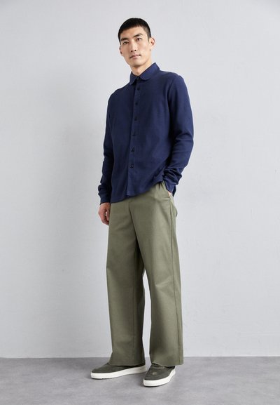 Navy blue button-up shirt with a collar, paired with olive green wide-leg trousers and gray sneakers. Simple design and relaxed fit.