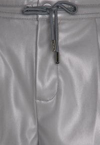 Pantalon en cuir gris avec une texture lisse, fermeture à cordon avec accents métalliques et détail de poche latérale.