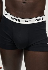 Κοντινό πλάνο ενός ατόμου που φοράει μαύρα μποξεράκια Nike με λευκή μέση που έχει μαύρα λογότυπα Nike και σύμβολα swoosh.