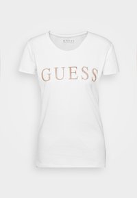 Hvid bomulds t-shirt med rund halsudskæring og korte ærmer, med "GUESS" trykt i roseguld glimmer over brystet.