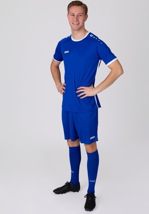 Blaues Fußballtrikot aus leichtem Material; mit weißen Akzenten, Logo auf der Brust und passenden Socken. Das Modell steht selbstbewusst.