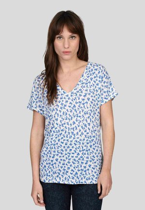 Blouse blanche à col en V avec un motif floral bleu, manches courtes, tissu léger, coupe décontractée et une texture subtile.