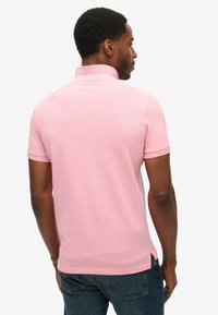 Koszulka polo z jasnoróżowego materiału, krótki rękaw, z ribbowanym kołnierzykiem. Posiada boczne rozcięcia i dopasowany krój. Noszona z ciemnoniebieskimi dżinsami.