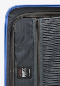 Black travel suitcase interior featuring mesh pocket, zippers, and a label. Soft blue trim contrasts with the dark fabric and textures.