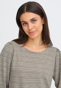Blouse marron à motifs avec un col rond, des manches bouffantes et un design en grille texturé. Tissu lisse aux tons neutres.