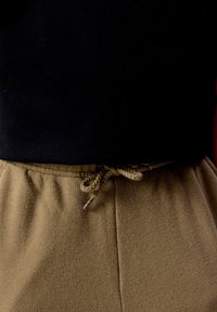 Beige värviliste dressipükste lähivõte, millel on seotud nöörvöökoht, kombineeritud musta särgiga.