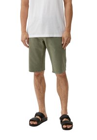 Zielone bawełniane szorty z bocznymi kieszeniami, wprost skrojone, z lekko wyblakłym wykończeniem, zestawione z czarnymi sandałami z regulowanymi paskami.