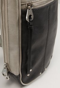 Czarna i szara skórzana torba z zamkiem błyskawicznym, srebrnymi akcentami i dekoracyjnymi ćwiekami, o teksturowanym wykończeniu i eleganckim designie.