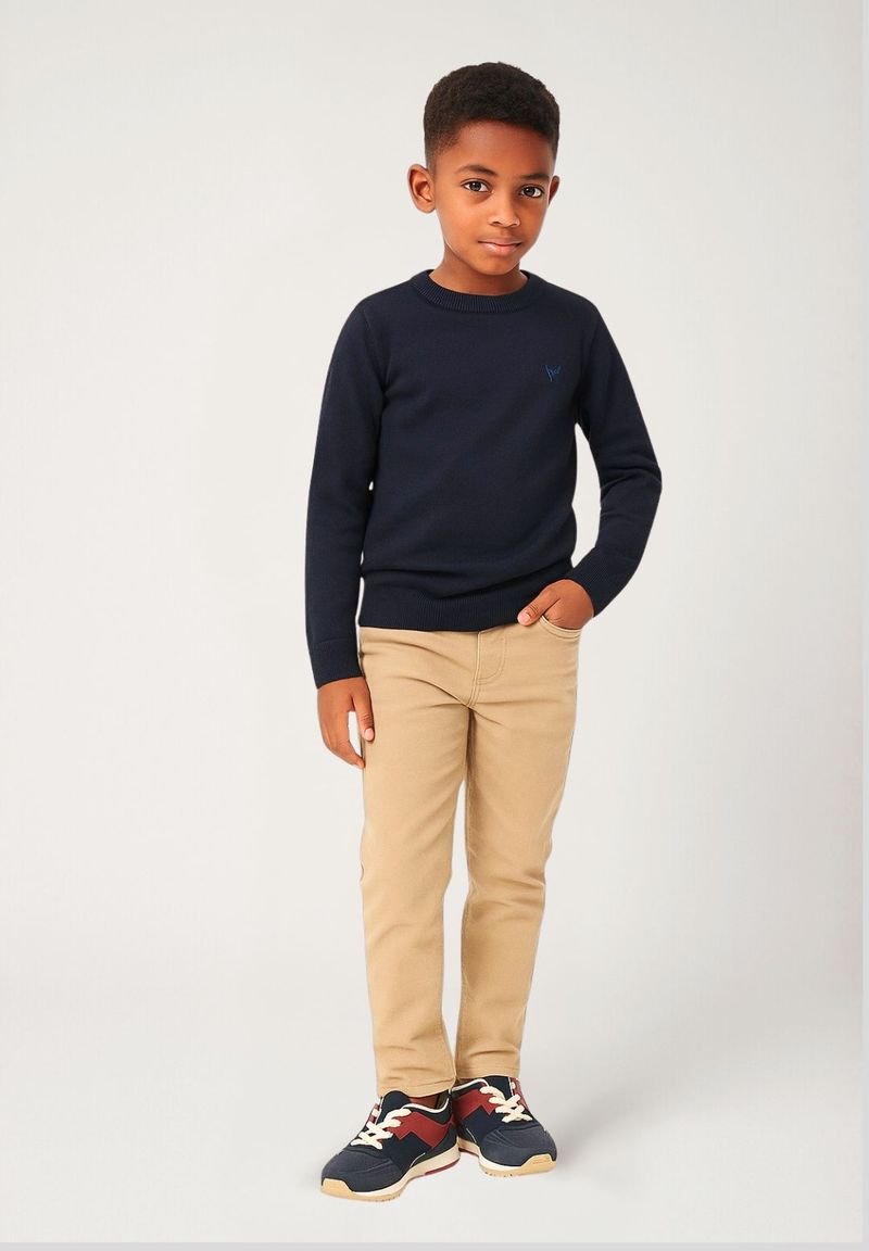 Modra pletena jopica s okroglim izrezom, bež kavbojke in modri športni copati z rdečimi in belimi akcenti. Jopica ima majhen detajl logotipa.