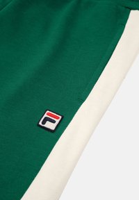 Grön bomullströja med ett vitt sidostråk, med en broderad Fila-logotyp i röd, blå och vit på vänster sida.