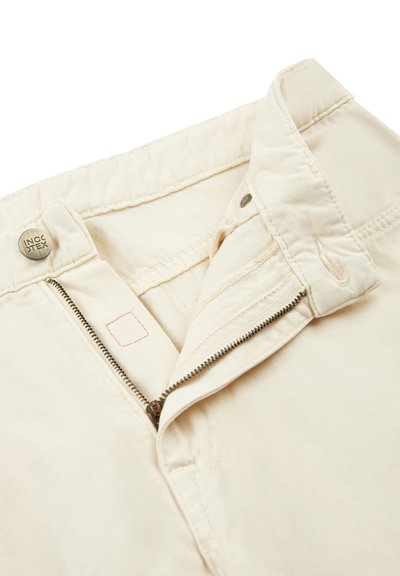 Pantalones de algodón beige con cremallera y botón de metal. Presentan una textura suave y costuras visibles a lo largo de la cintura y la cremallera.