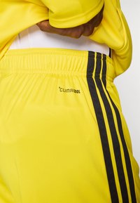 Κίτρινο αθλητικό σορτς με μαύρη πλαϊνή ρίγα και λογότυπο "CLIMACOOL", με ελαστική μέση και λεία, ελαφριά υφή.