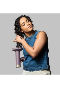 Hårføner med en lavendel-farget kropp, gullaksenter og en teksturert dyse. Modellen har på seg en jeans uten ermer, og viser frem stilige krøllete hår.