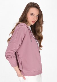 Roze zip-up hoodie met een capuchon, zijsplitten en geribde manchetten. Gemaakt van zacht materiaal, met een ontspannen pasvorm en subtiele glans.